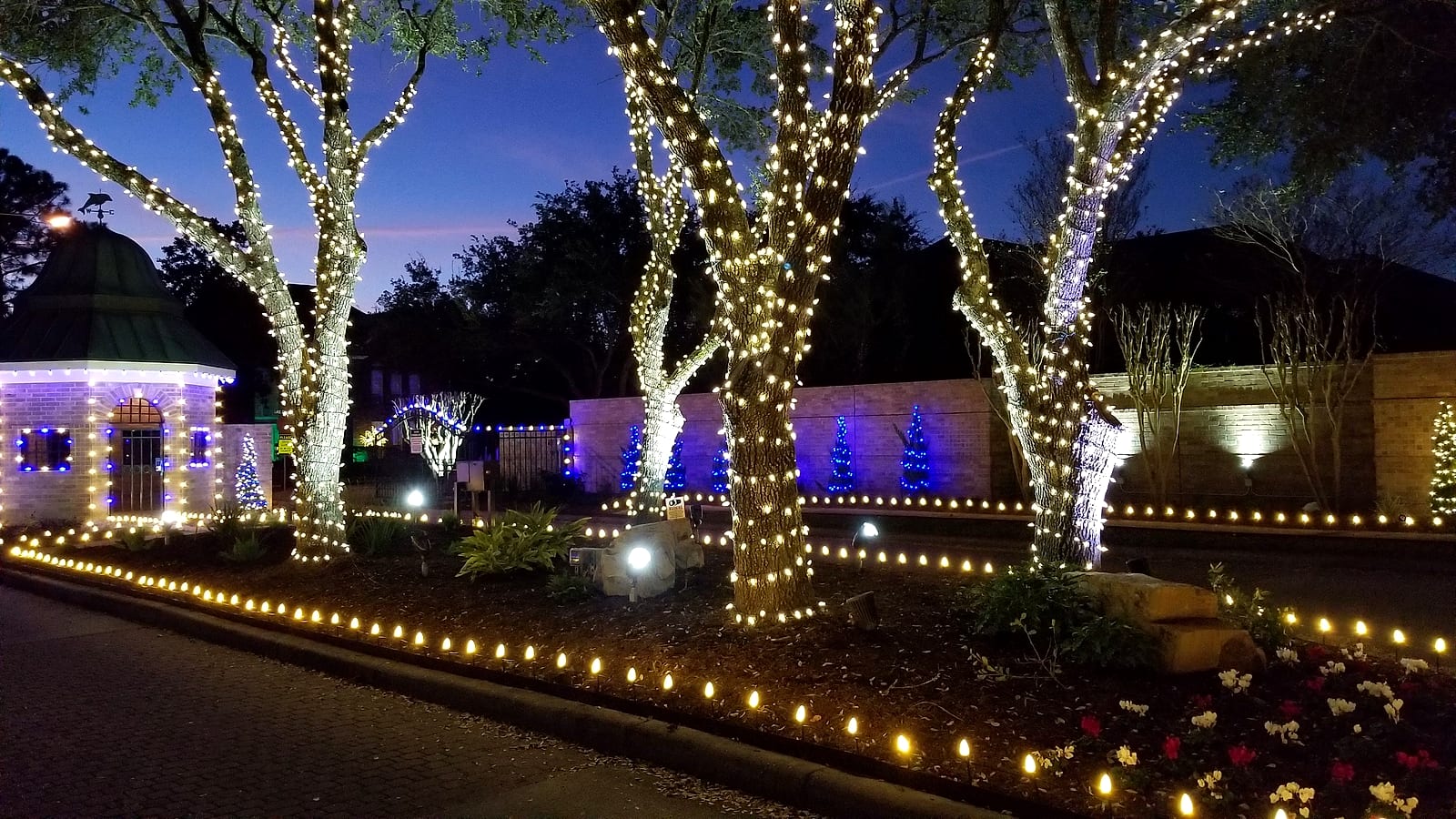 Wrapped oak trees, a lit gazebo and pathway lights at an estate entrance