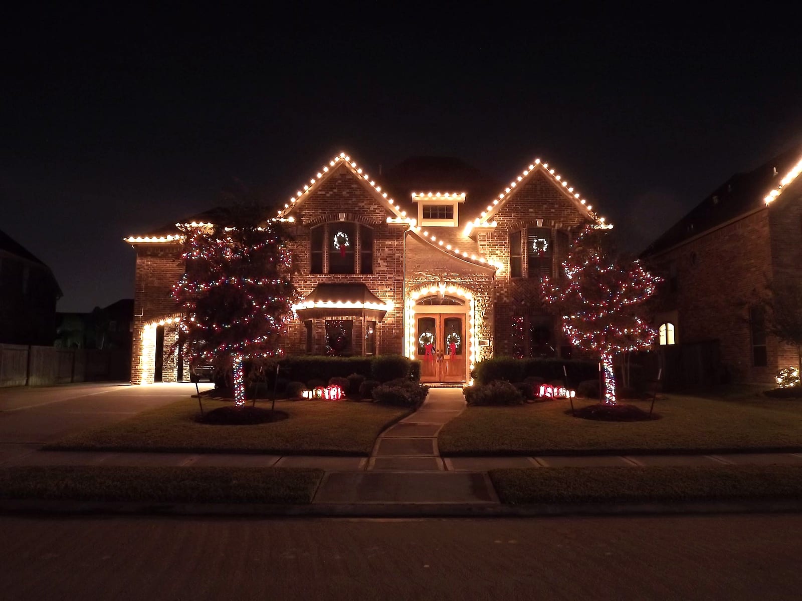 Two-story home with wrapped trees and a lit arched front door