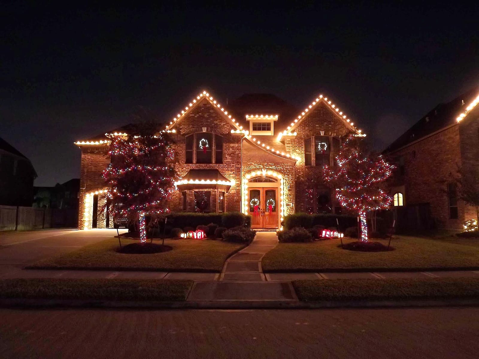 Warm white roofline with two wrapped trees and a lit walkway
