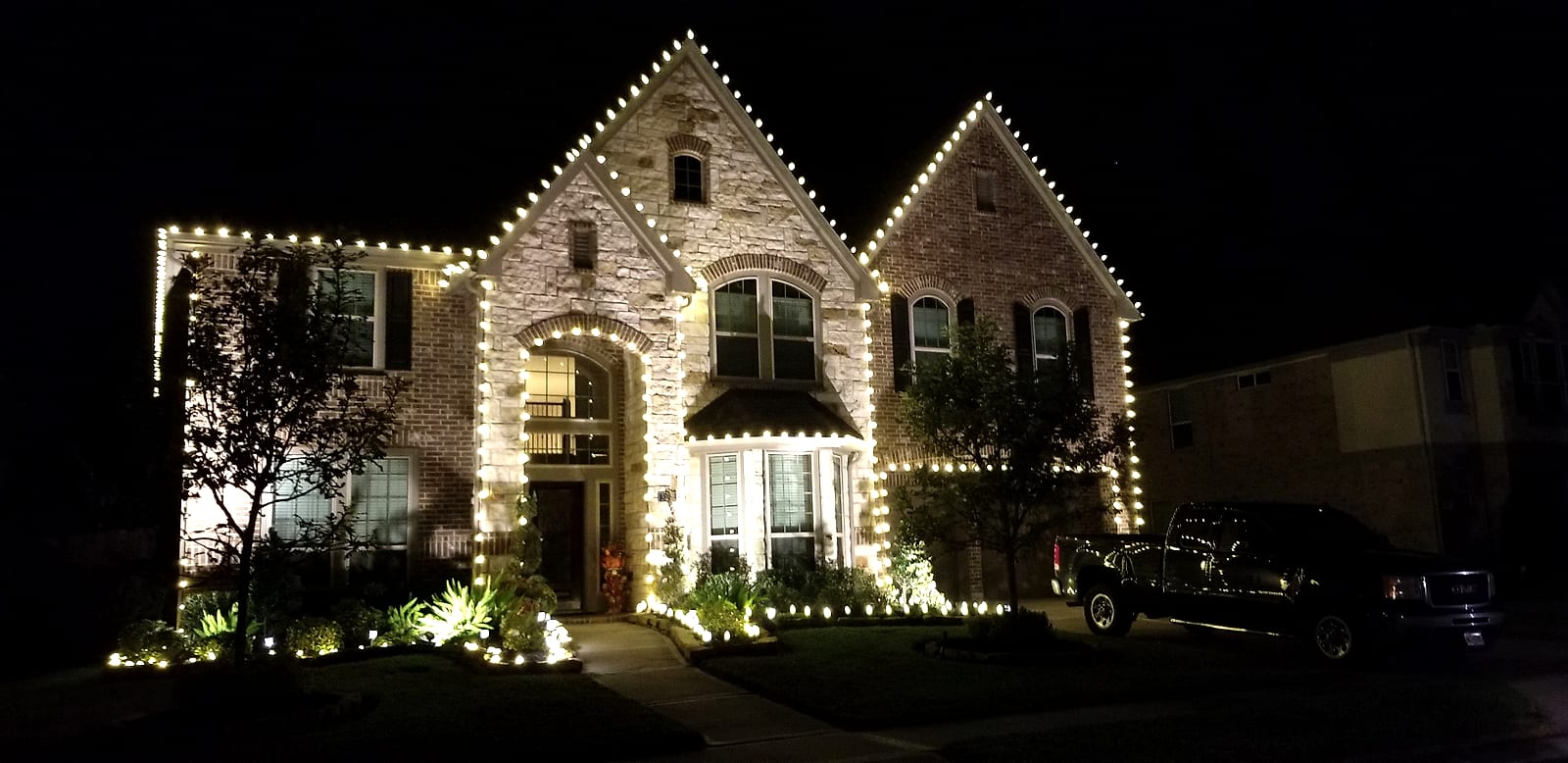 Warm white lights on a two-story stone and brick home